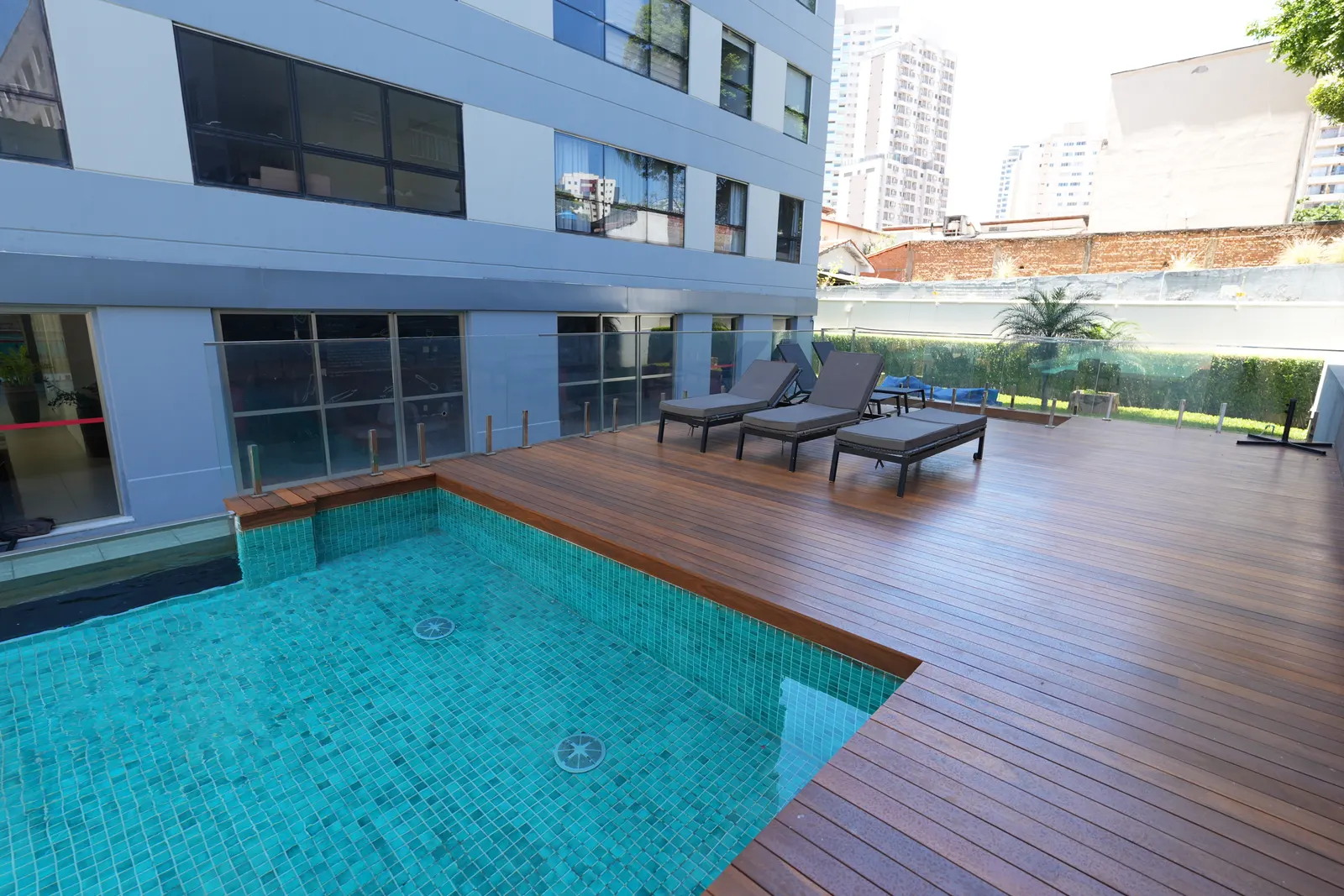 Deck de madeira em volta da piscina do Terraza, com espreguiçadeiras e prédio ao fundo